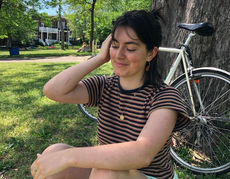 Zoé Bailly-Stetson sits under a tree, with her bicycle