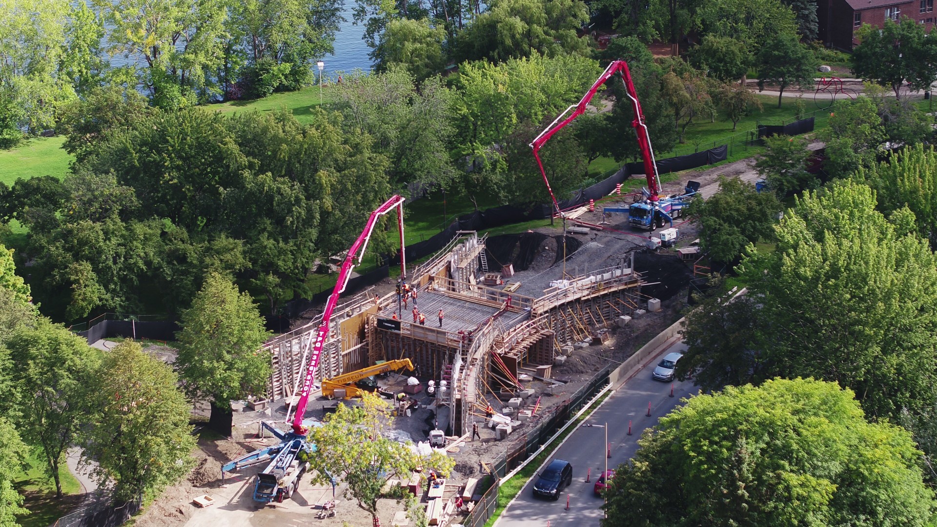 Ariel view of the bridge being constructed. Two red cranes dominate the action.