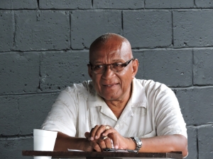 Paul Keens-Douglas sits at a desk with a cup of coffee.