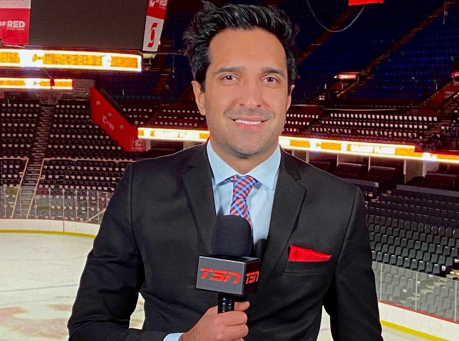 Salim Valji holds a microphone, reporting from a hockey game.
