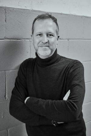 black and white photo of Yanick Létourneau, standing with his arms crossed, wearing a turtleneck