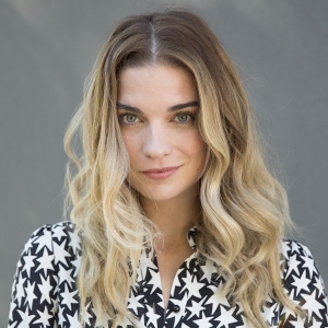 Annie Murphy smiles ambiguously, wearing a black and white blouse with stars on it.