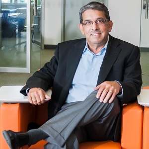 Karna Gupta, wears a suit, sitting on a bright orange chair