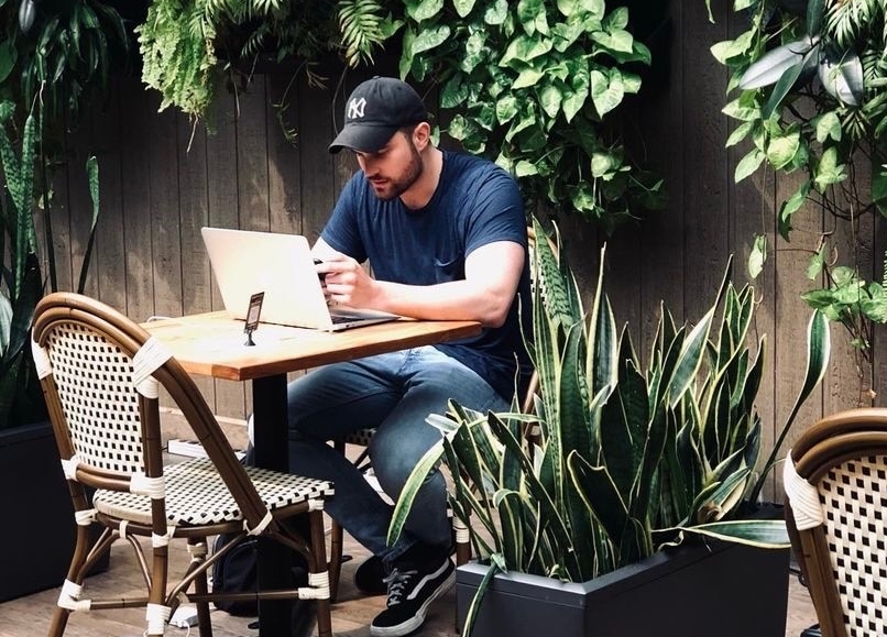Steven Regimbal works at his laptop in an outdoor space, surrounded by plants