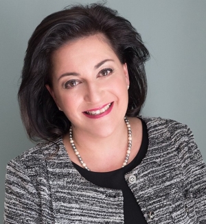 Headshot of a woman with short dark hair wearing a necklace and sweater, grey background