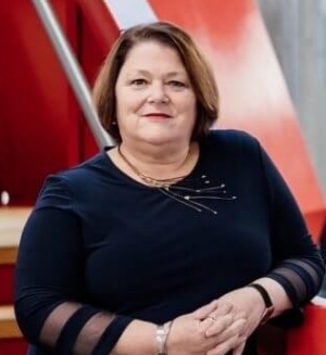 Woman with short brown hair and navy blue sweater stands in front of red staircase