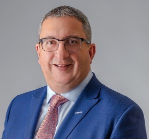 A man with glasses wearing a blue suit smiles for the camera.