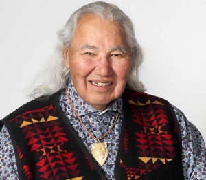 A man with long grey hair wears a cardigan over a button-up shirt.
