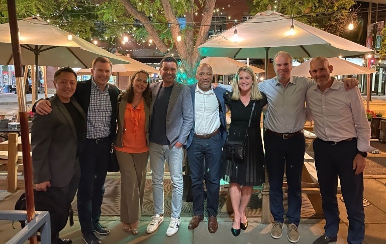 A group of people gather and pose for a photo outdoors at a restaurant terrace.