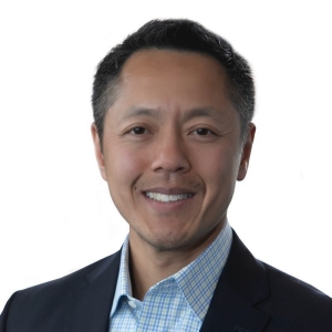 A man wearing a suit and with dark, short hair smiles for the camera.