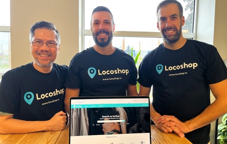 Three men wearing matching Locoshop T-shirts stand in front of an open laptop