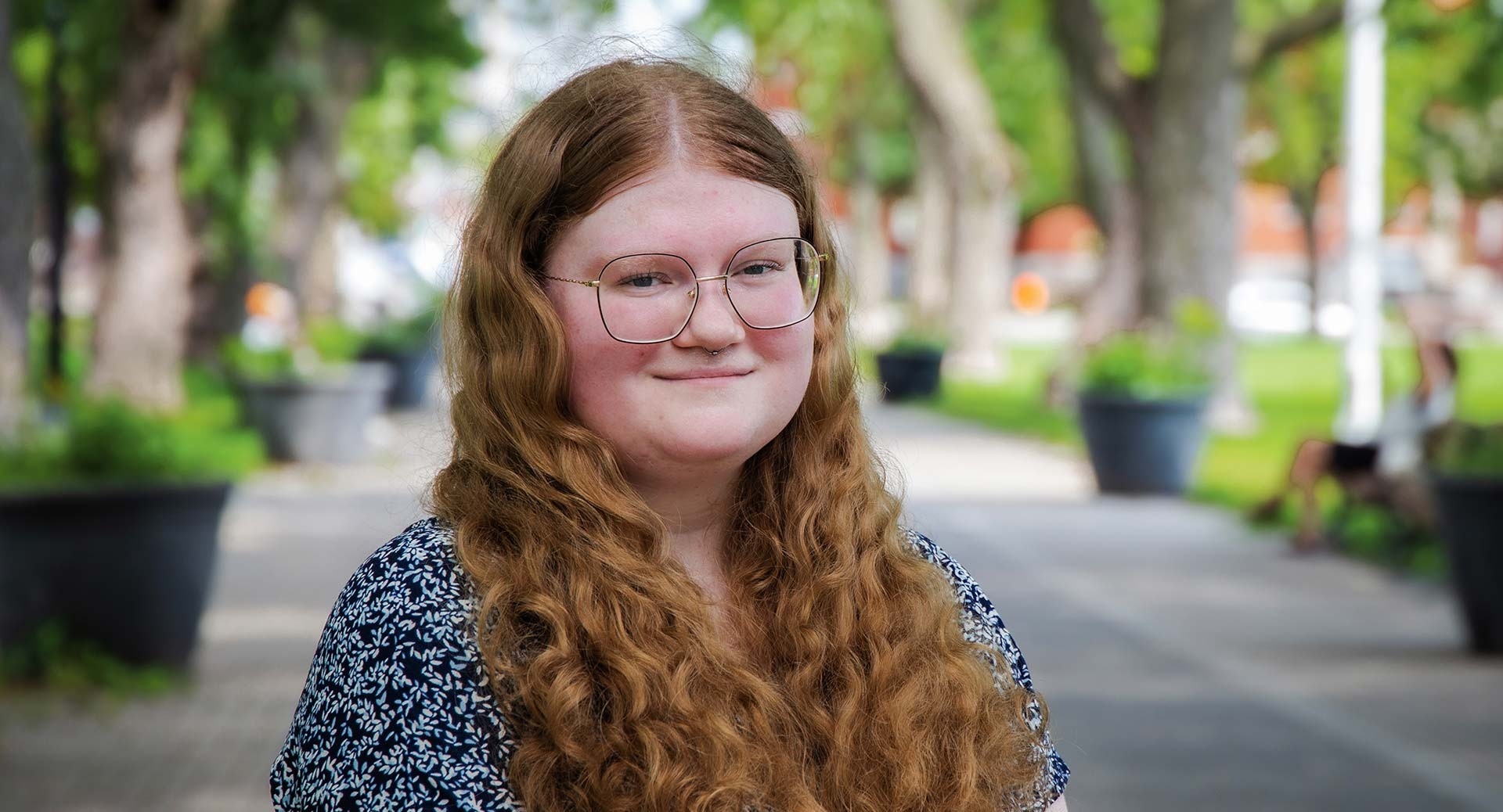 Bridget has red hair and glasses. She is outside and wears a black and white dress