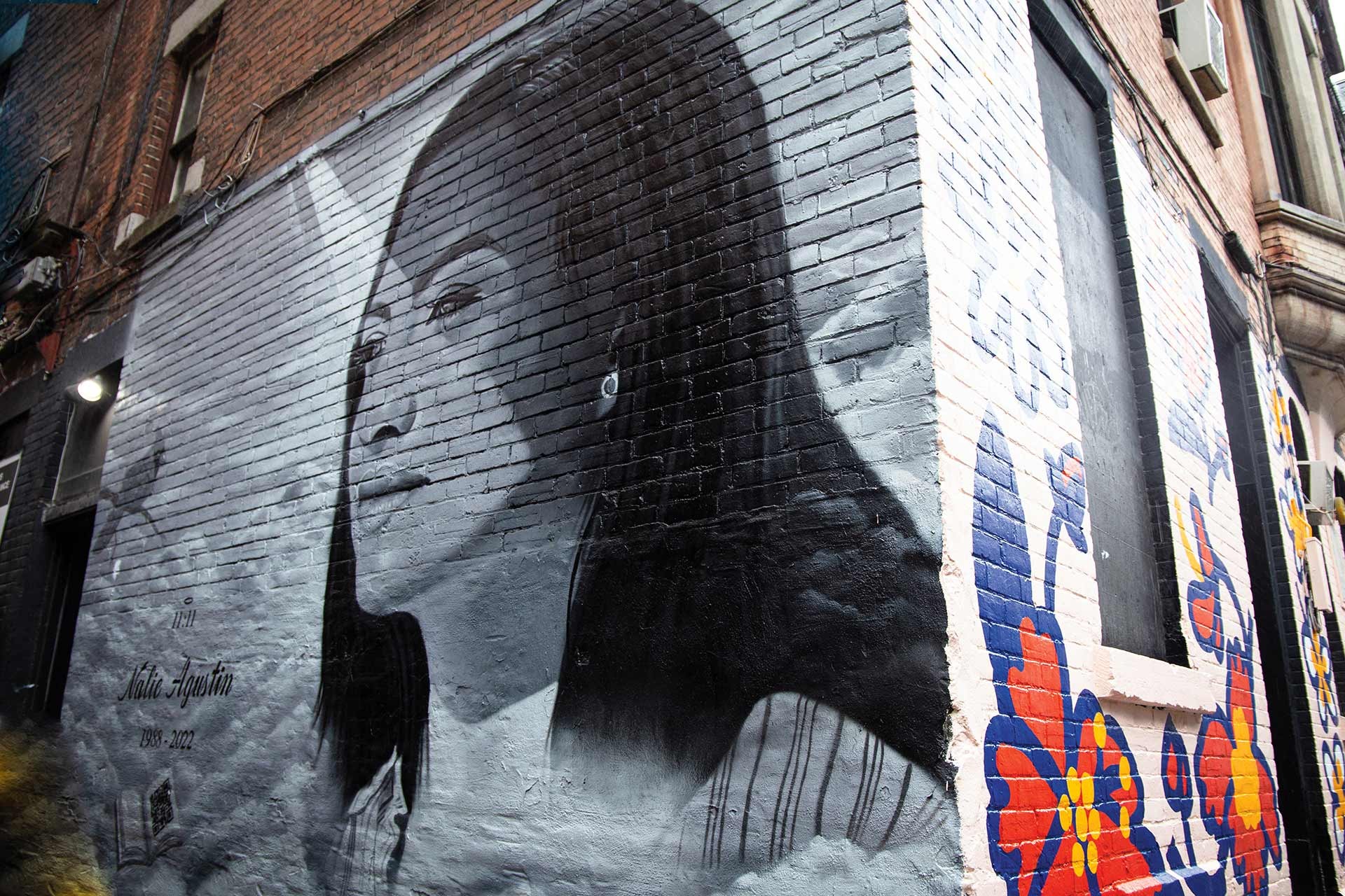 A painting of a young woman with long dark hair on a brick wall