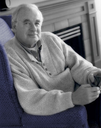 Portrait of a man wearing a sweater, seated in front of a fireplace