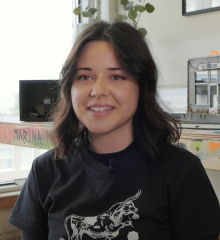 Artist Marina Totino, who has short black hair and wears a black t-shirt, sits in her art studio.