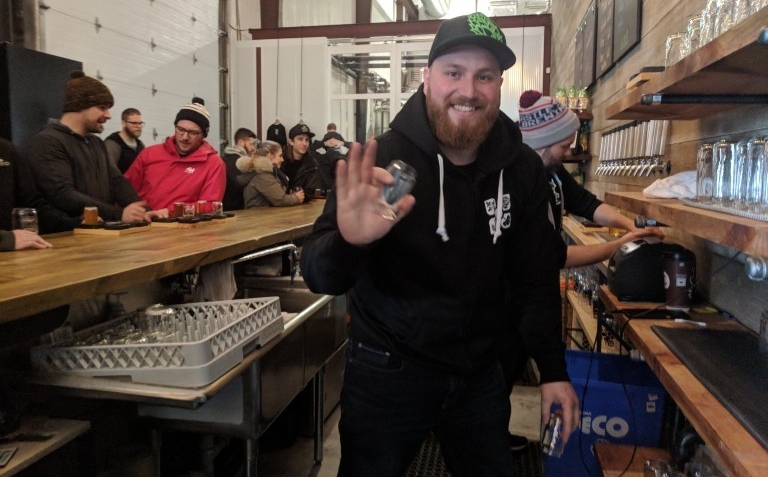 A man with a black baseball cap and a dark hoodie works behind the counter of a bar