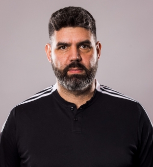 Karam Al-Hamdani has dark hair and a beard, and wears a black soccer jersey