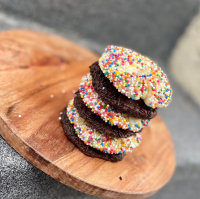 A stack of chocolate and vanilla sprinkled cookies sit on a round, wooden plate