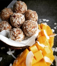 Beige-coloured energy balls covered in desiccated coconut sit next to a cut up mango