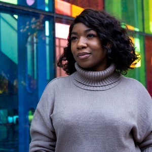 A woman with medium-length black hair wears a turtleneck sweater