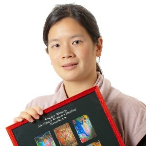 A woman wears her black hair in a ponytail and holds a frame in her hands