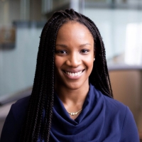 Hawa Kerita has long, black braided hair and is smiling, wearing a blue navy blue top and silver necklace