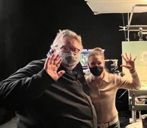 Two people in masks stand on the set of a film and wave at the camera