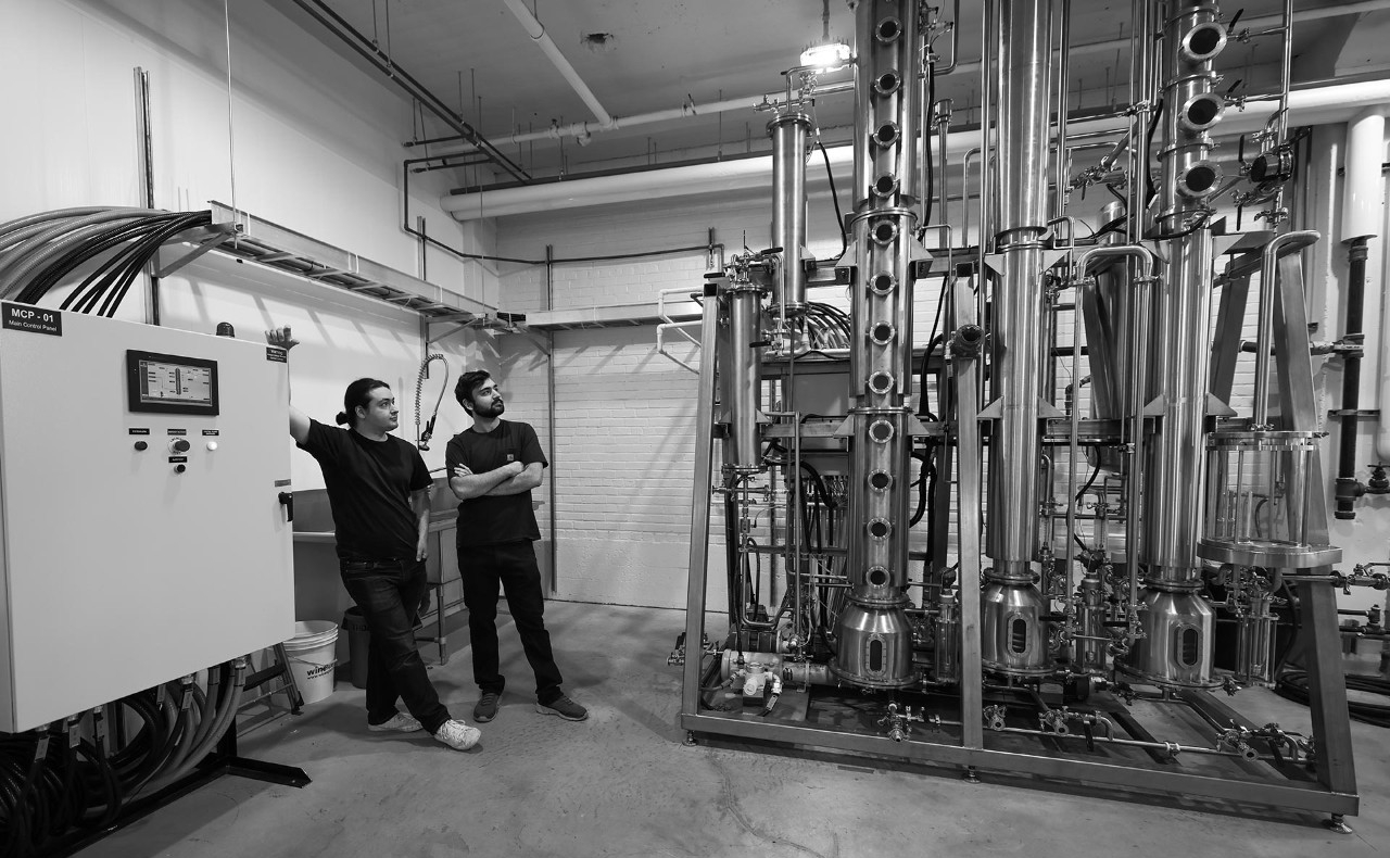 A black and white photo of two young men standing to the left of a distillery