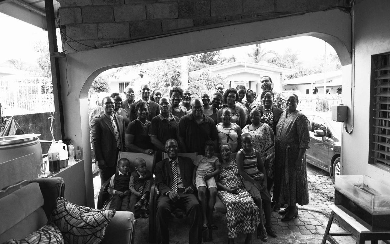 A group of several family members stand and smile under a patio roof covering 