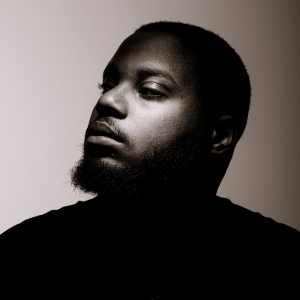 A black and white portrait of the artist in low light and a soft spotlight under his eye.