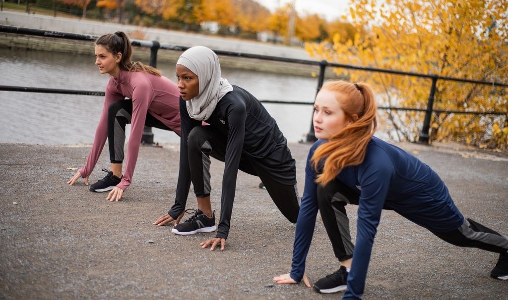 Models wearing modest athletic clothing in runner's start position on pavement next to canal