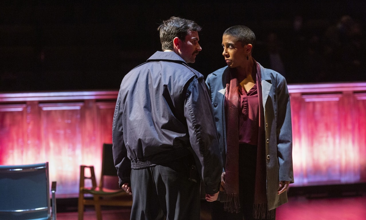 A man and woman stand face-to-face on stage, staring closely into each other's eyes.