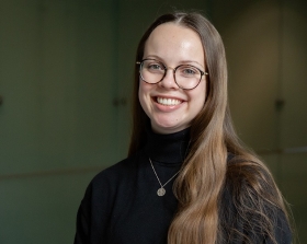 A colour portrait of Victoria D'Amours, wearing a sweater, glasses and a necklace