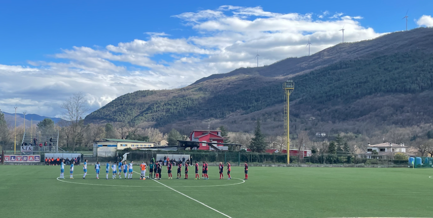 Soccer players congregate on the pitch with mountains in the background