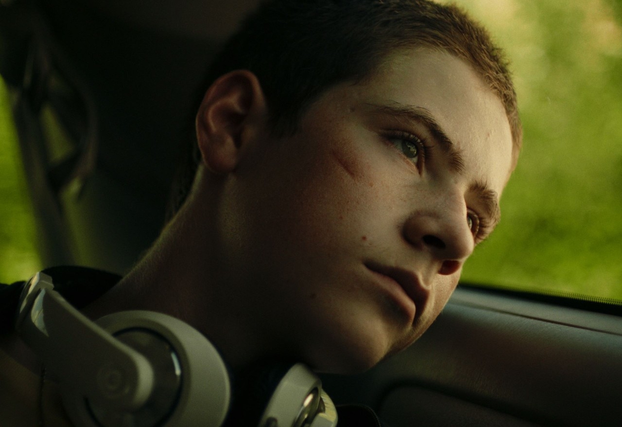 Man wearing headphones around his neck, leaning head against window 