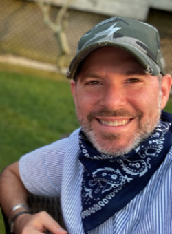 Portrait of a smiling man, wearing a white T-shirt, navy handkerchief around his neck and a baseball cap 