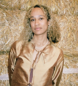 Portrait of a woman with black curly hair wearing a pastel colour-blocked top and light-coloured jeans