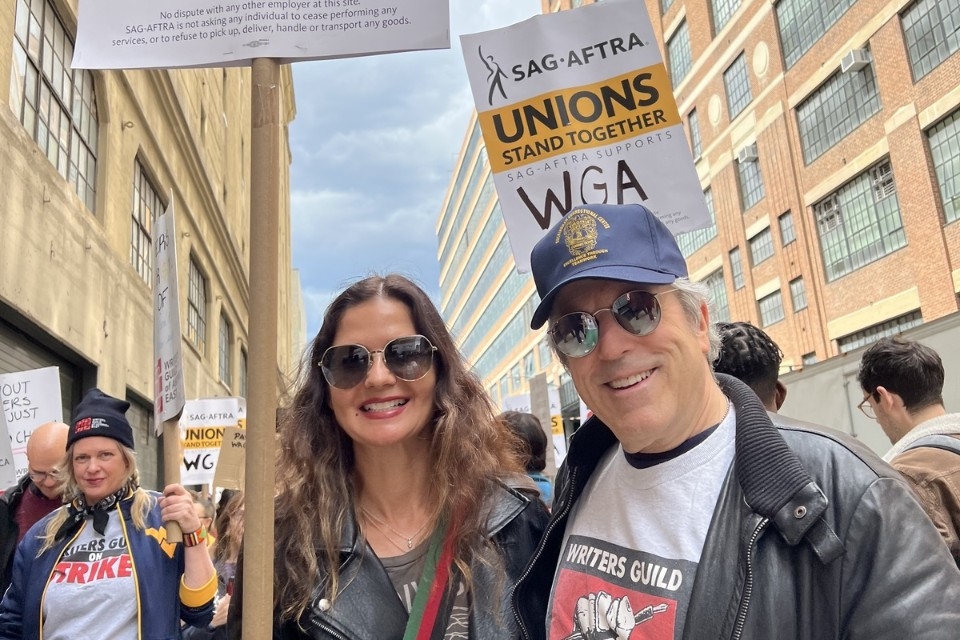 René Balcer and Jill Hennessy stand with a crowd holding picket signs.