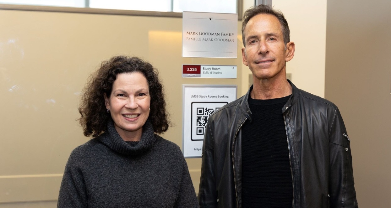 A dark-haired man wearing a leather jacket stands next to a woman with dark, curly hair in a charcoal sweater