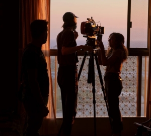 A silhouette of Joyce Joumaa, director of photography William Albu, BFA 20, filiming on a balcony overlooking an expansive, hazy view