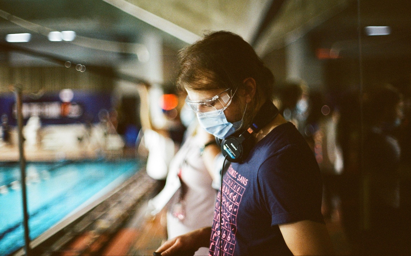 Mattias Graham wears headphones, a t-shirt and surgical mask while on set, standing next to a swimming pool.