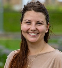 A woman with long brown hair and a beige shirt smiles at the camera