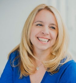 A smiling woman with blonde hair is wearing a blue blouse