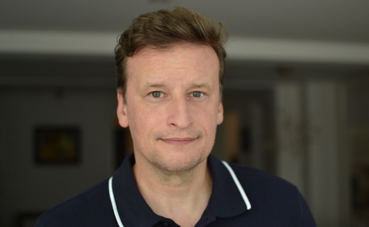 Headshot of a man with brown hair wearing a navy blue polo shirt with a white stripe around the collar.