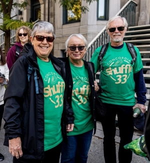 Three people wearing green t-shirts and glasses stand on sidewalk