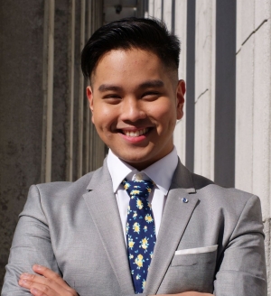 Student in suit and tie stands with arms crossed