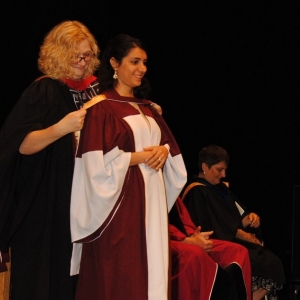 Maryam Zakeryfar stands on stage for her convocation robing ceremony 