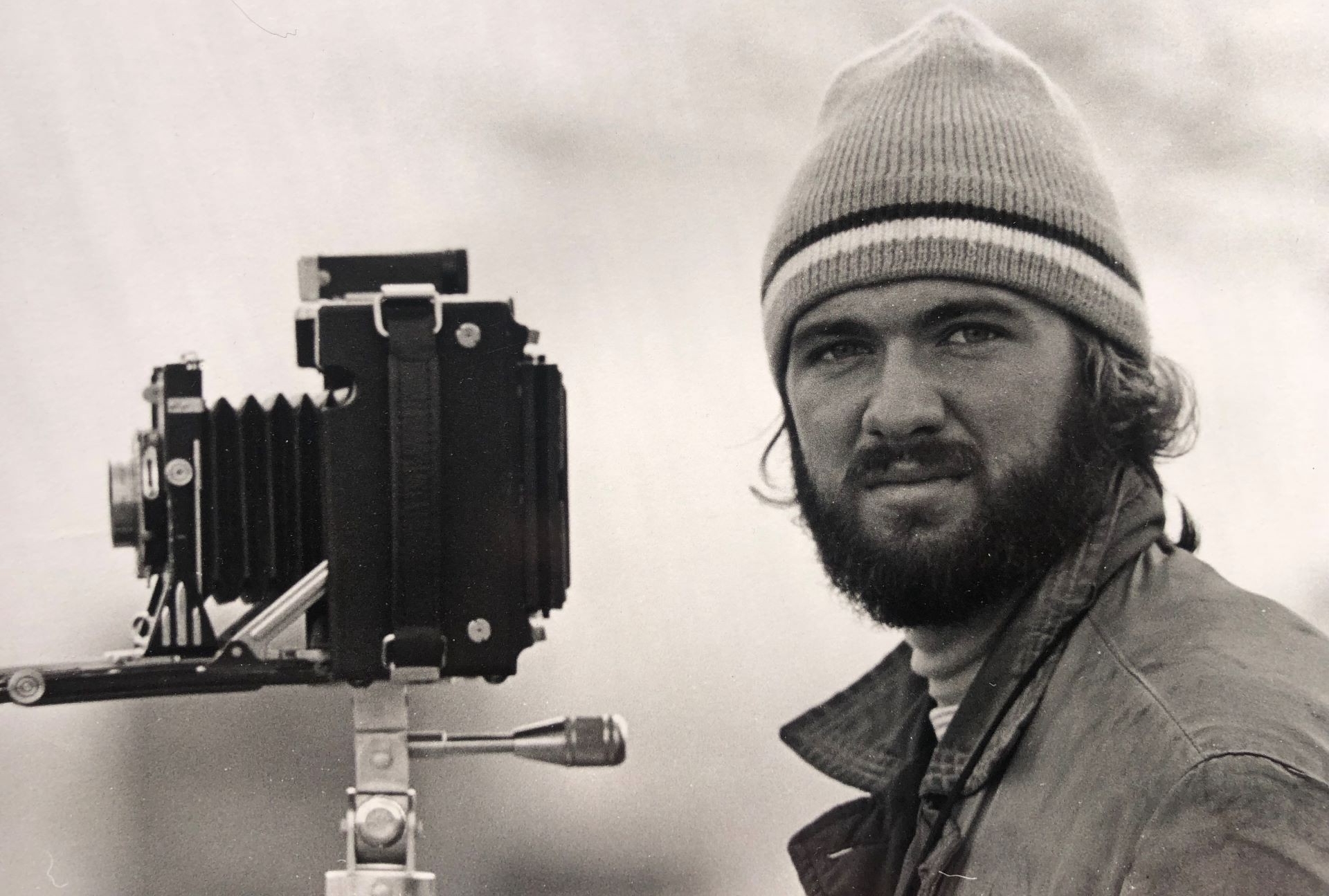 black and white photo of young, bearded man with a mid-century folding camera