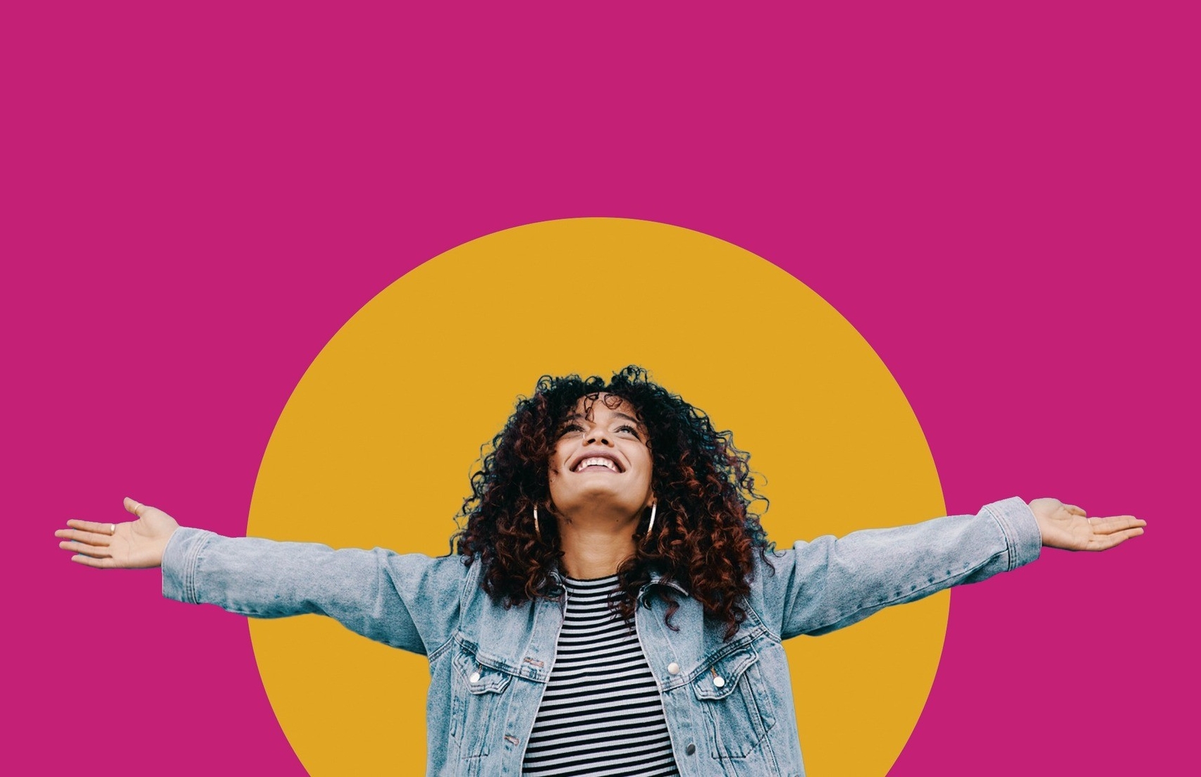 An exuberant woman with curly hair is smiling broadly with her eyes closed, arms wide open as if embracing the world. She's wearing a striped top underneath a denim jacket. The background is vibrant fuchsia with a large, mustard yellow circle positioned behind her, giving a lively and joyful composition to the image.