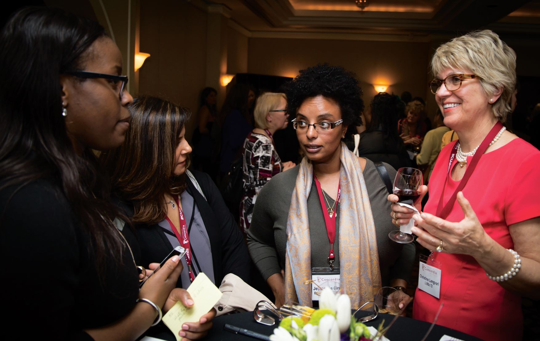 Four women stand around a cocktail table, speaking to one another